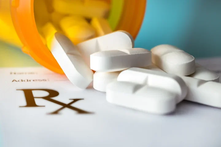 Pills: white tablets spilling from an orange bottle onto an Rx prescription form.