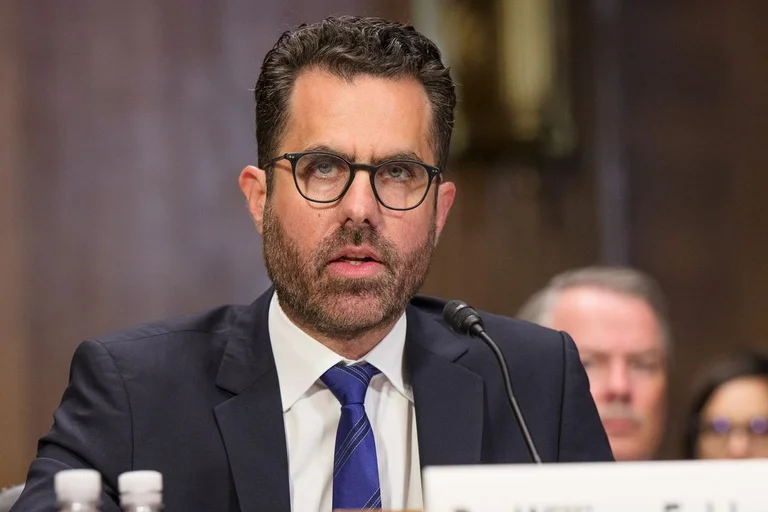 Person in a suit behind a congressional desk and mic