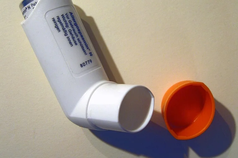 White asthma inhaler with orange cap placed on a flat surface.
