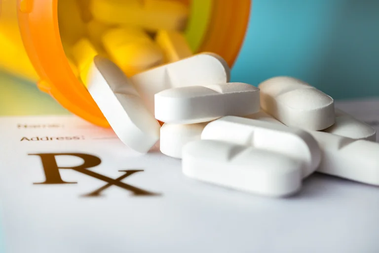 Pills: white tablets spilling from an orange bottle onto an Rx prescription form.