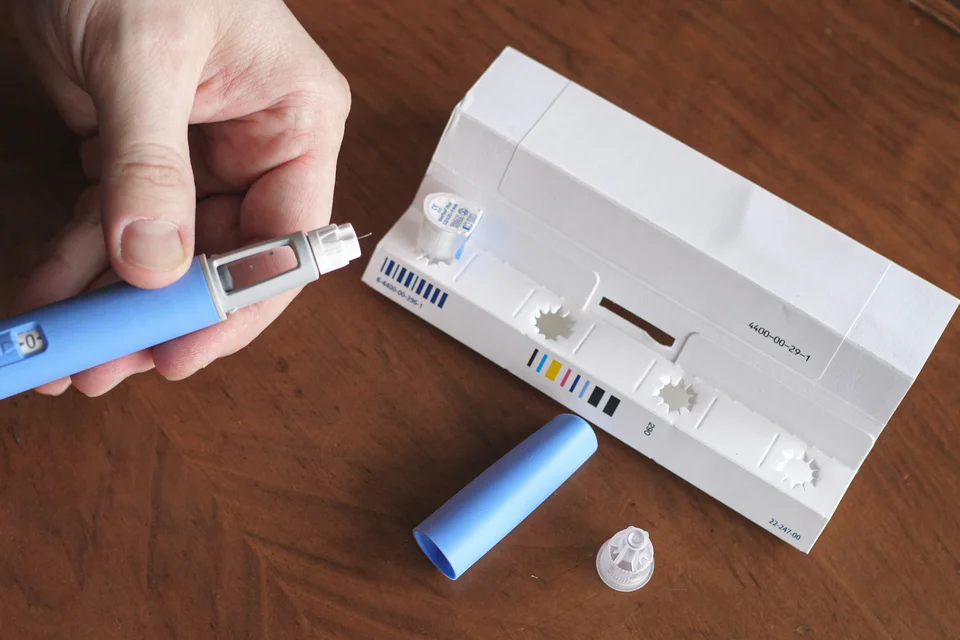 Hand holding a blue injection pen next to testing supplies on a wooden surface