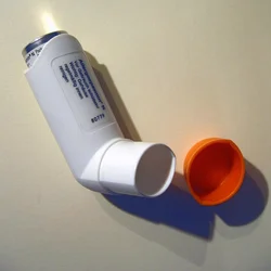 White asthma inhaler with orange cap placed on a flat surface.