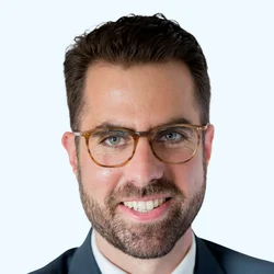 headshot of smiling person with glasses in a suit and white background