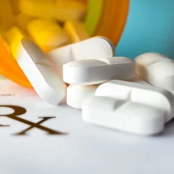 Pills: white tablets spilling from an orange bottle onto an Rx prescription form.